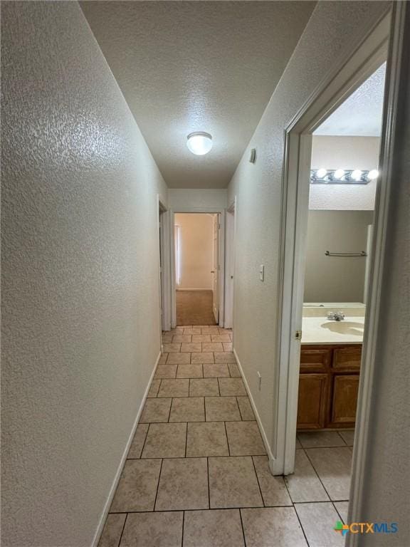 hall with sink, a textured ceiling, and light tile patterned flooring