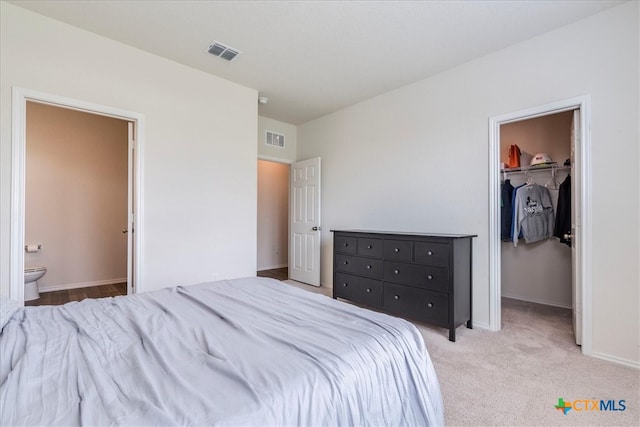 bedroom featuring ensuite bath, light carpet, a walk in closet, and a closet