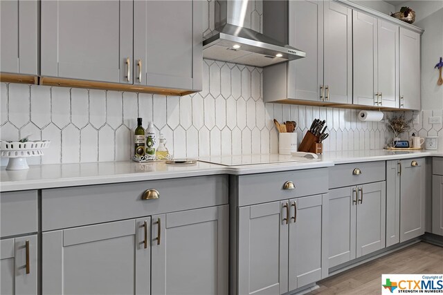 kitchen featuring light hardwood / wood-style floors, stovetop, backsplash, gray cabinets, and wall chimney range hood