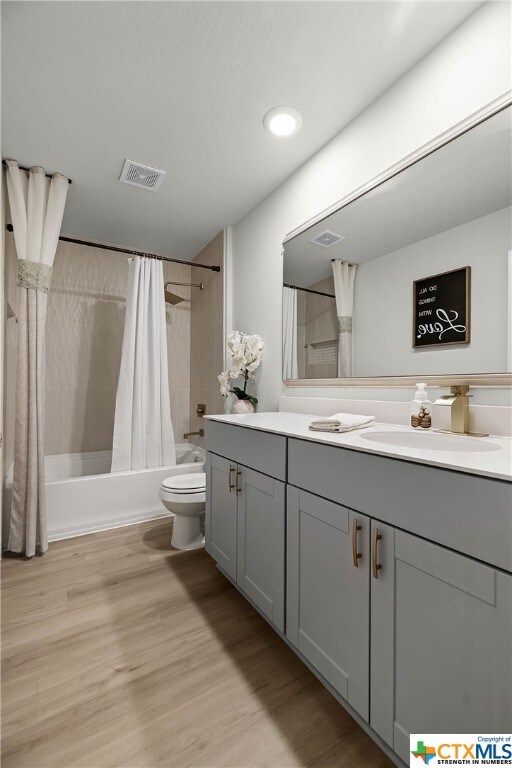 full bathroom featuring hardwood / wood-style flooring, vanity, shower / bath combination with curtain, and toilet