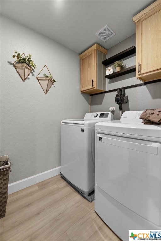 clothes washing area with cabinets, light hardwood / wood-style floors, and independent washer and dryer