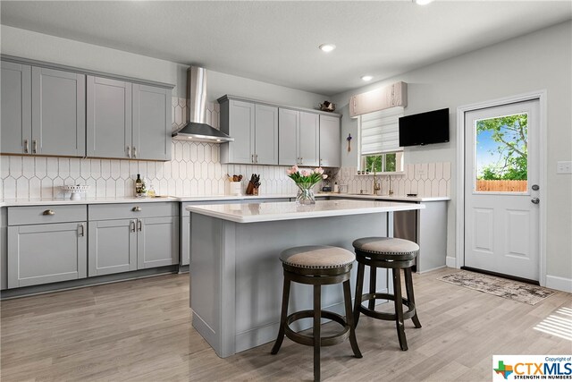 kitchen featuring gray cabinetry, wall chimney range hood, decorative backsplash, and light hardwood / wood-style floors