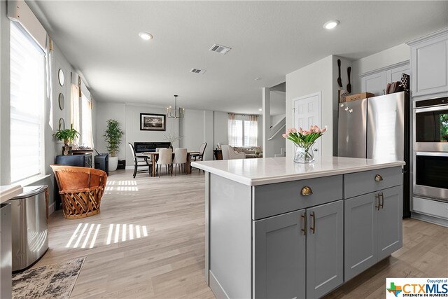 kitchen with appliances with stainless steel finishes, light wood-type flooring, a kitchen island, gray cabinetry, and pendant lighting