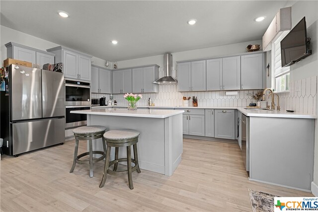 kitchen with light hardwood / wood-style flooring, wall chimney range hood, a center island, and stainless steel appliances