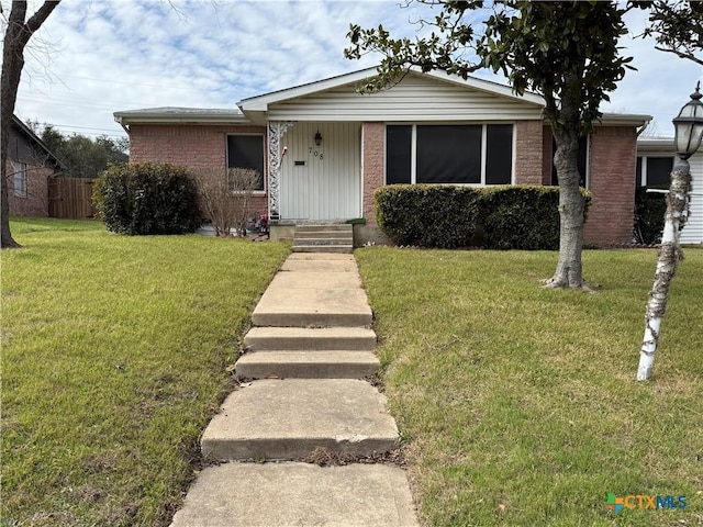 view of front facade with brick siding, a front yard, and fence