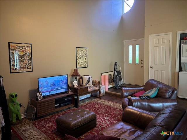 living area featuring baseboards, stacked washer / dryer, a high ceiling, and wood finished floors