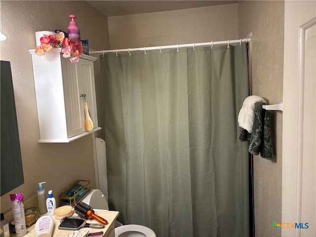 full bath with a shower with curtain, toilet, and a textured wall