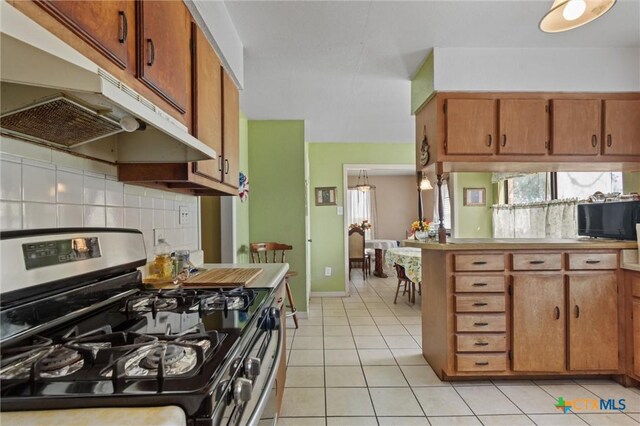 2080 Allison Rd, Martindale, TX 78655 - kitchen featuring stainless steel range with gas stovetop, under cabinet range hood, backsplash, brown cabinetry, and light tile patterned floors