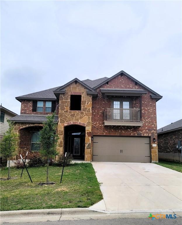 view of front of property featuring brick siding, concrete driveway, a front yard, a garage, and stone siding