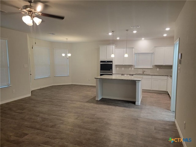 kitchen with light stone countertops, dark wood finished floors, a sink, white cabinets, and a center island