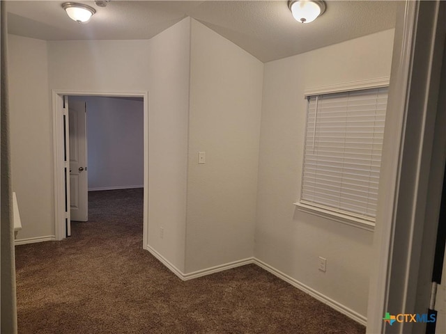 empty room with baseboards, a textured ceiling, and dark carpet