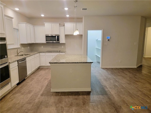 kitchen featuring light stone countertops, visible vents, a sink, stainless steel appliances, and a center island