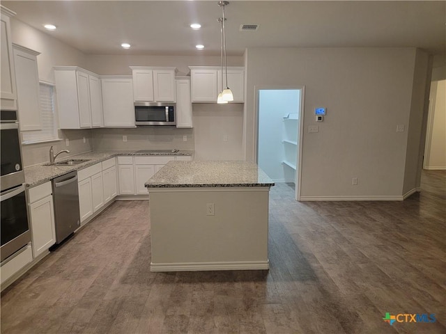 kitchen with a sink, light stone counters, a kitchen island, and stainless steel appliances