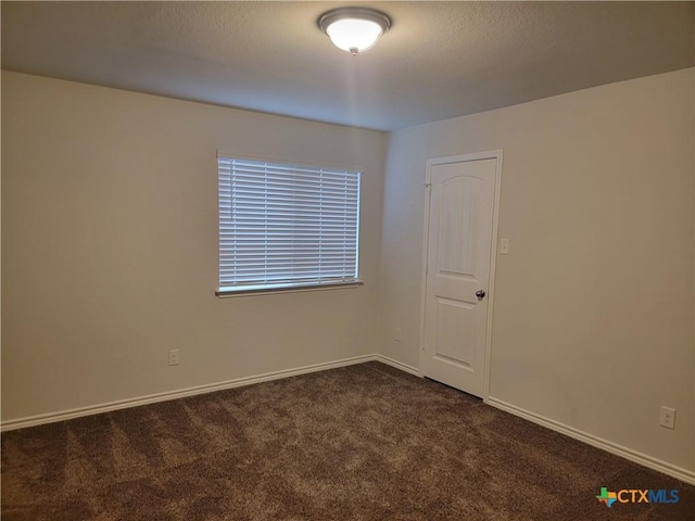 empty room with dark carpet, a textured ceiling, and baseboards