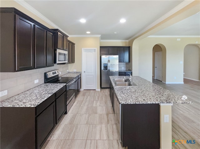 kitchen featuring crown molding, appliances with stainless steel finishes, decorative backsplash, sink, and a kitchen island with sink