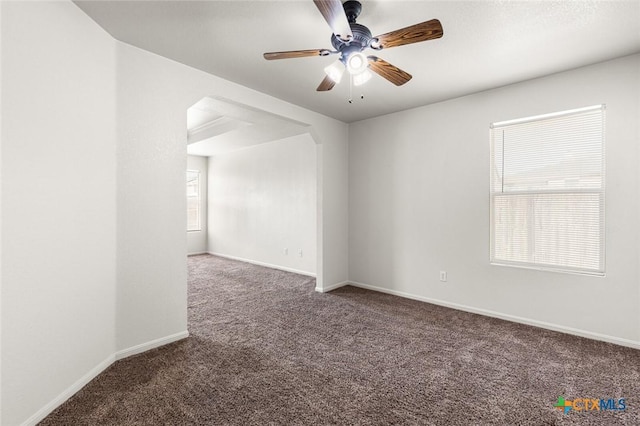 empty room featuring carpet floors, arched walkways, a healthy amount of sunlight, and baseboards