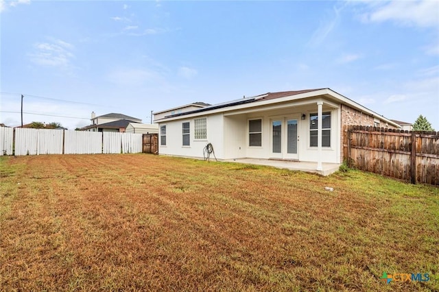 back of property with a patio area, a fenced backyard, roof mounted solar panels, and a yard