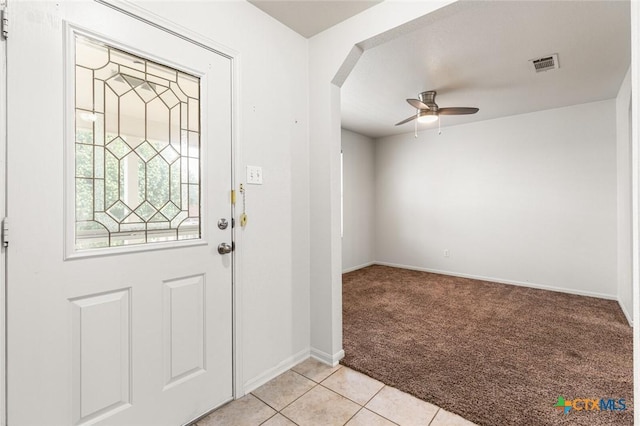 foyer entrance featuring arched walkways, light tile patterned floors, light carpet, visible vents, and a ceiling fan