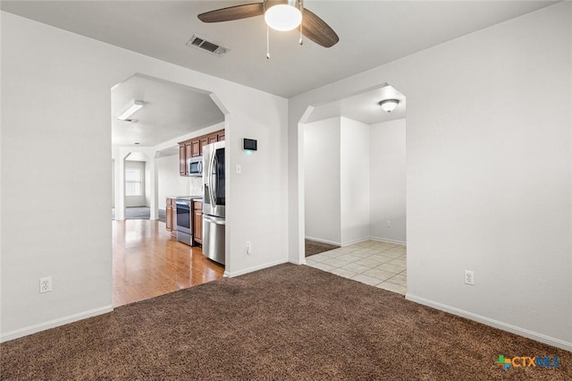 empty room featuring baseboards, visible vents, arched walkways, a ceiling fan, and light colored carpet