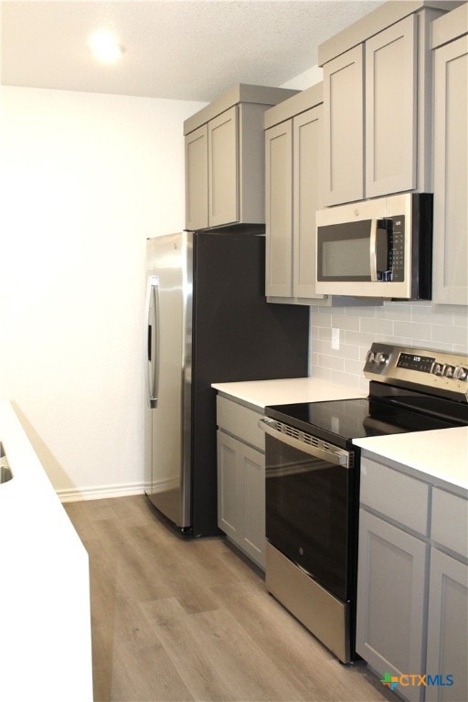 kitchen featuring gray cabinets, light wood-type flooring, backsplash, and appliances with stainless steel finishes