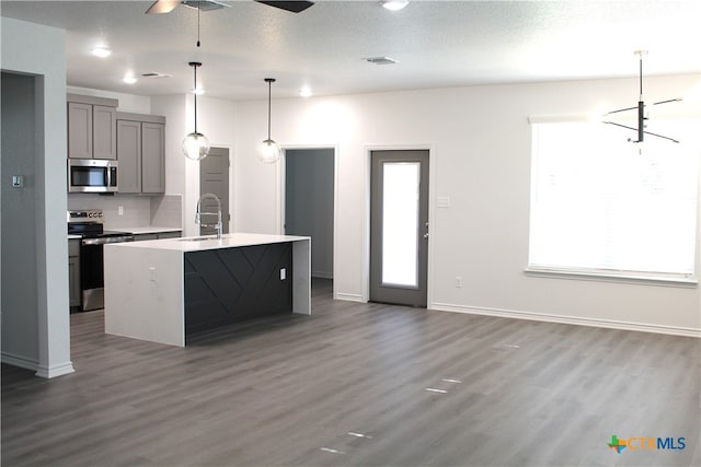 kitchen with gray cabinetry, stainless steel appliances, dark wood-type flooring, decorative light fixtures, and an island with sink