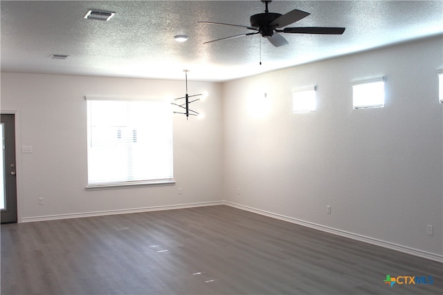 unfurnished room with a textured ceiling, a wealth of natural light, dark hardwood / wood-style flooring, and ceiling fan with notable chandelier