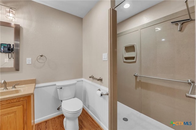 full bathroom featuring wood finished floors, toilet, vanity, a walk in shower, and wainscoting