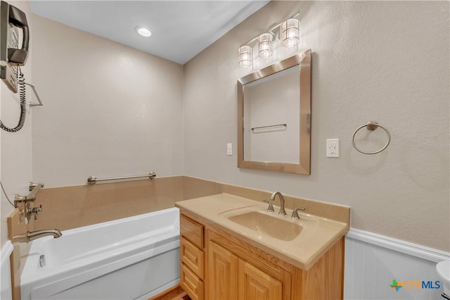 bathroom featuring a bath, a wainscoted wall, and vanity