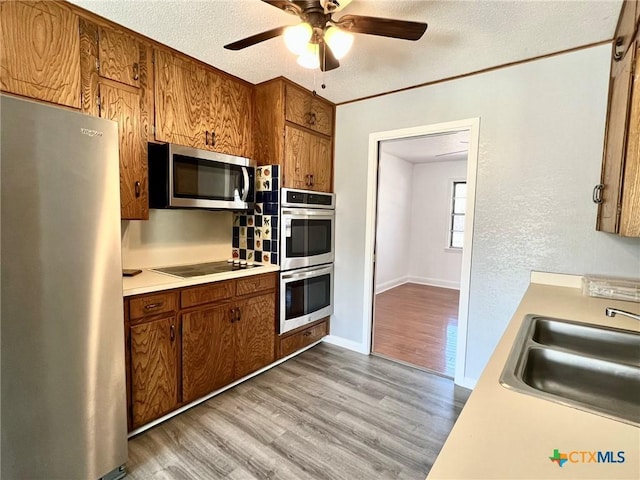 kitchen with a textured ceiling, stainless steel appliances, a sink, light countertops, and light wood-type flooring