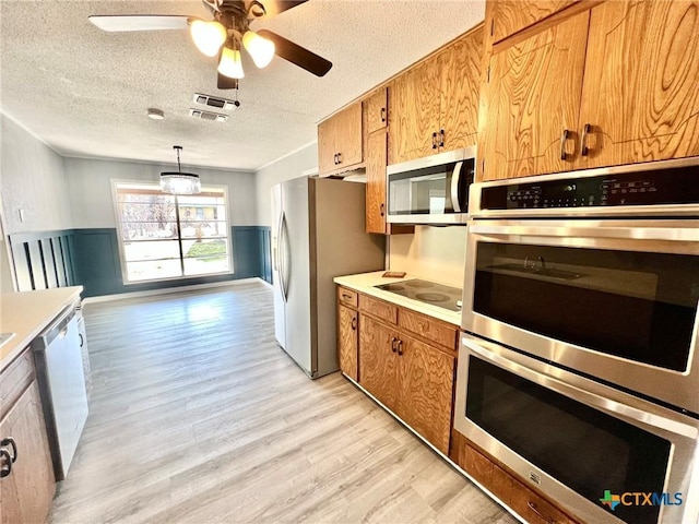 kitchen featuring appliances with stainless steel finishes, wainscoting, light wood-style floors, and a textured ceiling