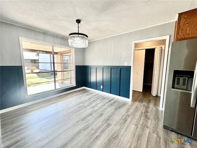 unfurnished room with crown molding, a textured ceiling, wood finished floors, and wainscoting