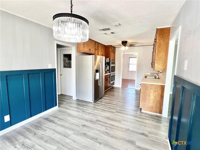 kitchen with light countertops, appliances with stainless steel finishes, light wood-style flooring, and brown cabinets