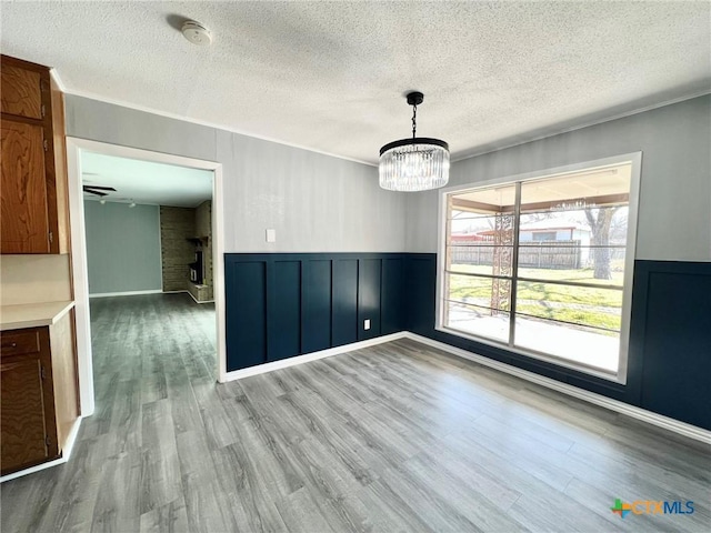 unfurnished dining area featuring a fireplace, a chandelier, wood finished floors, and wainscoting