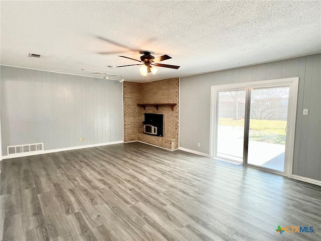 unfurnished living room featuring a brick fireplace, wood finished floors, visible vents, and a ceiling fan