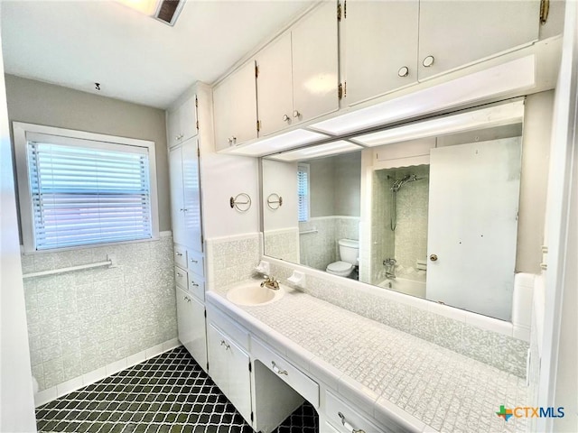 full bath with toilet, a wainscoted wall, vanity, tile walls, and shower / washtub combination