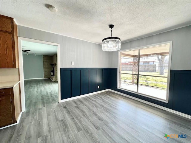 unfurnished dining area with a wainscoted wall, wood finished floors, a textured ceiling, and a notable chandelier
