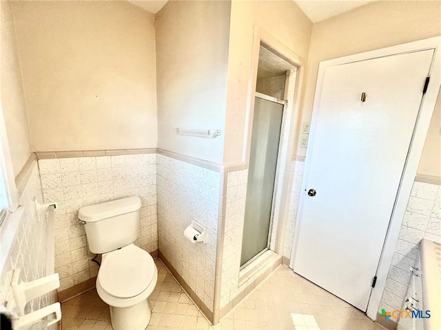 full bathroom featuring tile walls, a wainscoted wall, a shower stall, and toilet