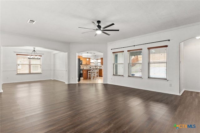 unfurnished living room with a wealth of natural light, arched walkways, dark wood finished floors, and ceiling fan with notable chandelier