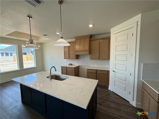 4018 Prairie Dr, Nolanville, TX 76559 - kitchen featuring a textured ceiling, dark wood-style flooring, hanging light fixtures, a kitchen island with sink, and light stone countertops