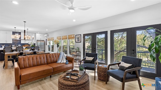 living room featuring french doors, light hardwood / wood-style floors, and ceiling fan with notable chandelier