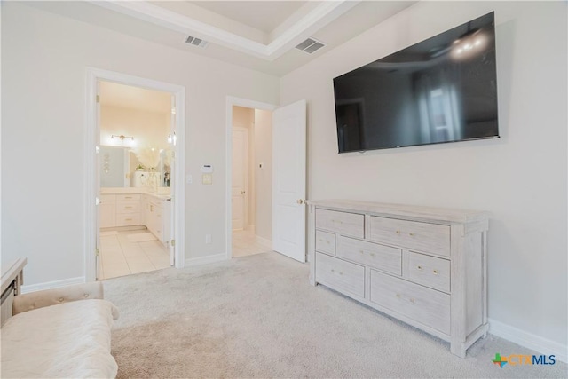 bedroom featuring light carpet, connected bathroom, and a raised ceiling