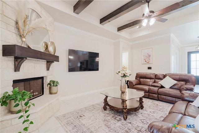 living room with ceiling fan, beam ceiling, a stone fireplace, and crown molding