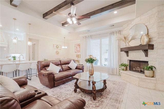 living room with beam ceiling, crown molding, a fireplace, and ceiling fan with notable chandelier