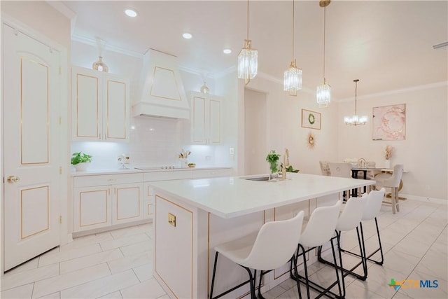 kitchen featuring sink, premium range hood, ornamental molding, and an island with sink