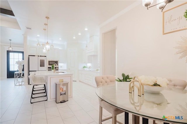 kitchen featuring built in microwave, pendant lighting, a center island with sink, white cabinets, and ornamental molding