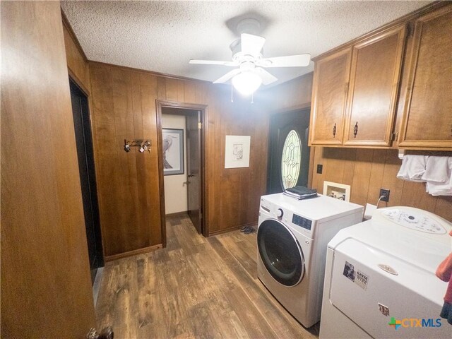 laundry room featuring cabinet space, washing machine and dryer, wood finished floors, wooden walls, and a ceiling fan