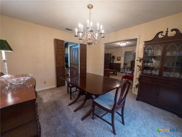 carpeted dining room with a chandelier and a textured ceiling