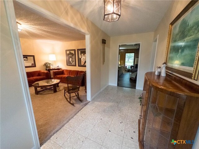 hallway featuring a textured ceiling, light floors, and baseboards