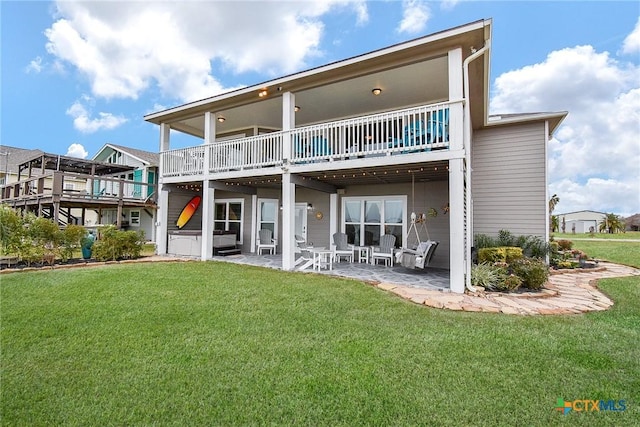 rear view of property featuring a wooden deck, a lawn, and a patio