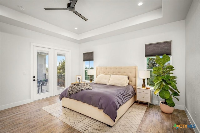 bedroom with baseboards, a tray ceiling, wood finished floors, and access to exterior